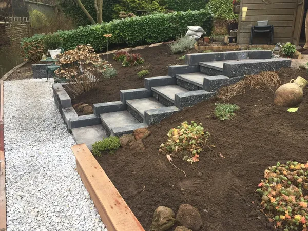 Voortuinmuurtje met bestrating in aanleg en getrapte plantenbakken.