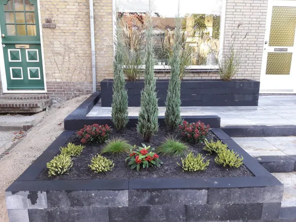 Voortuin met zwarte stenen plantenbakken en sierbeplanting bij entree.
