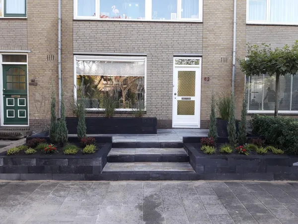 Voortuin met opstap, zwarte plantenbakken en tegelbestrating bij entree.