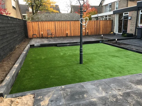 Houten overkapping met grijze tegelbestrating en stapstenen door kunstgras.