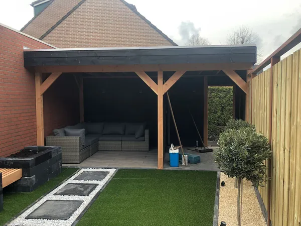 Verlichte tuin bij avond met tegelbestrating, lichtstrip en overkapping.