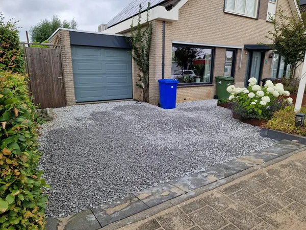Achtertuin met grijze betontegels en grindpad rondom gazon.