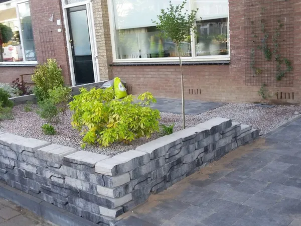 Voortuin met natuurstenen muurtje, klinkerbestrating en sierbeplanting.