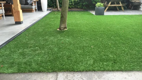Kunstgrasveld met aangrenzende grijze tegelbestrating onder overkapping.
