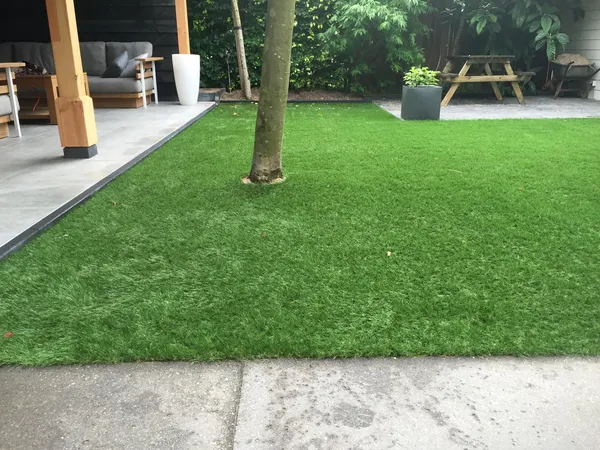 Kunstgrasveld met aangrenzende grijze tegelbestrating onder overkapping.