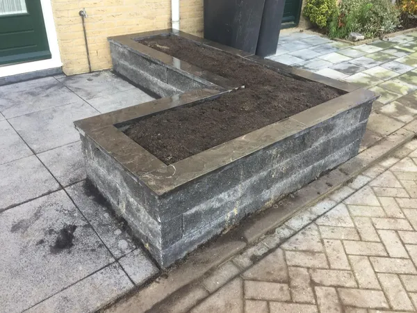 Verhoogde plantenbak van natuursteen op grijze tegelbestrating.