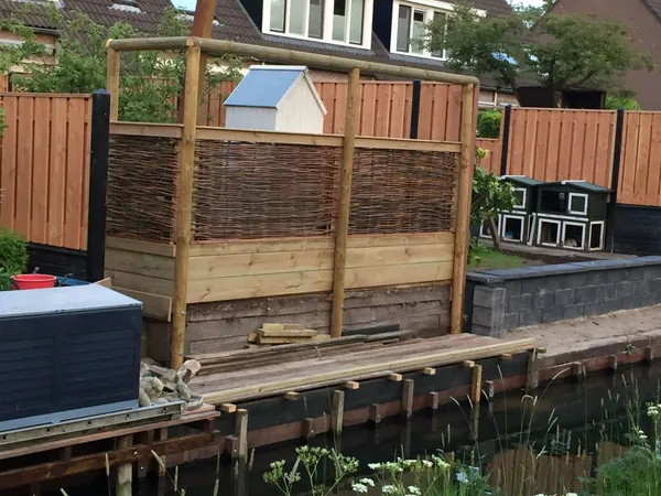 Houten schutting met wilgenscherm-vulling in aanbouw op vlonder aan het water.
