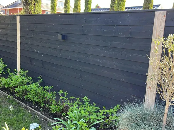 Zwarte houten schutting met horizontale planken en cederhouten staanders in tuin met beplanting.