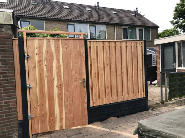 Cederhouten poort met aansluitende houten schutting en betonnen onderplaat tussen woningen.