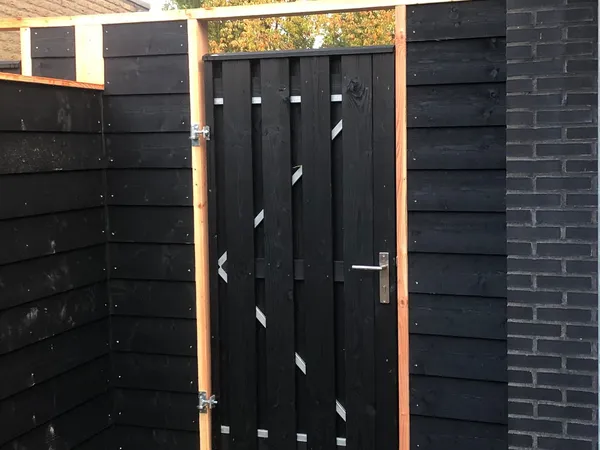 Zwarte houten poort met cederhouten frame en aansluitende schutting bij entree.