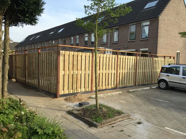 Nieuwe houten schutting met afdekplank langs parkeerplaats bij rijtjeswoningen.
