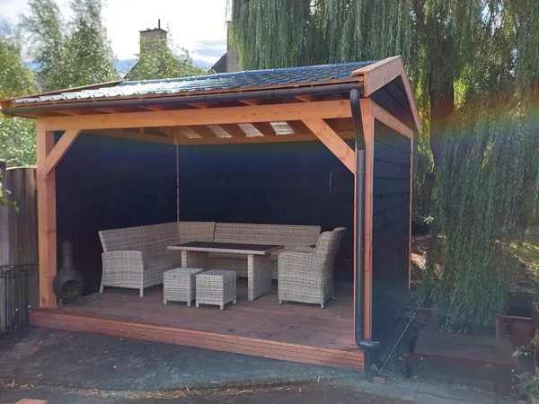 Houten overkapping met loungeset onder treurwilg.
