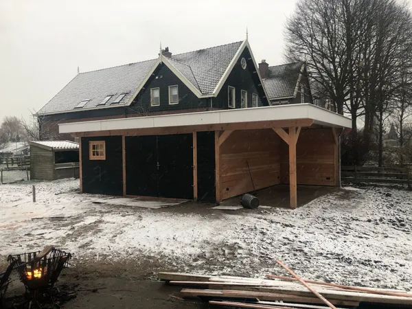 Grote zwarte schuur met overkapping in aanbouw in winterlandschap.