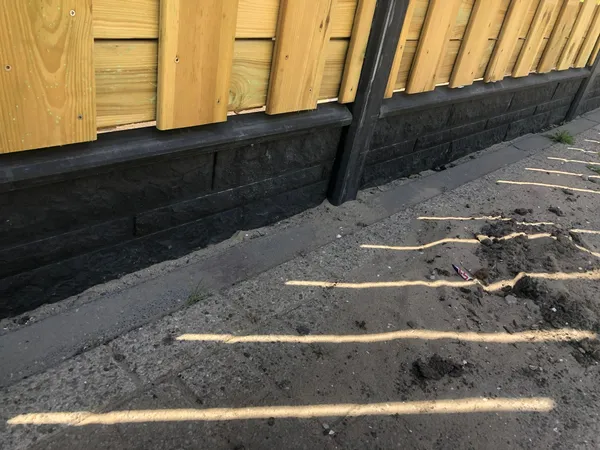 Detail van houten schutting met zwarte betonnen onderplaat bij aanleg.
