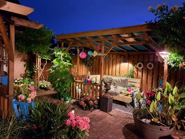 Sfeervolle tuin met houten pergola, bestrating en kleurrijke beplanting bij avondlicht.
