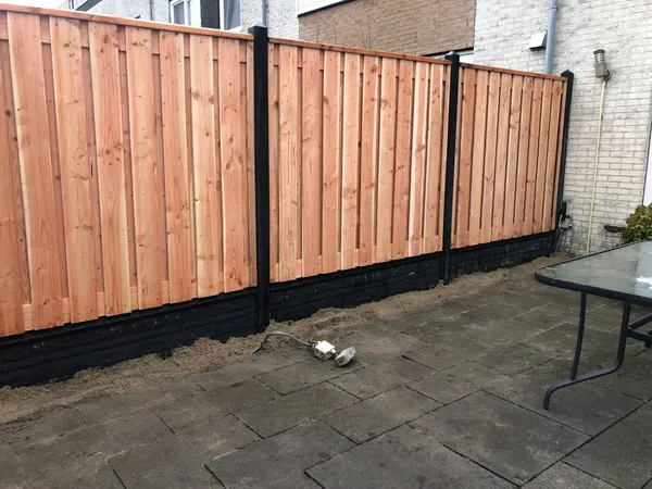 Houten schutting met zwarte betonnen palen en onderplaat op tegelterras.