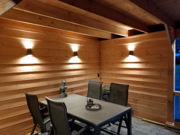 Sfeervol verlichte houten overkapping met eettafel en wandlampen.