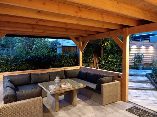 Houten overkapping met loungeset en sfeerverlichting in de schemering.
