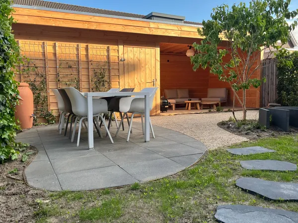 Houten overkapping met cederhouten wand, eetset en ronde tegelbestrating.