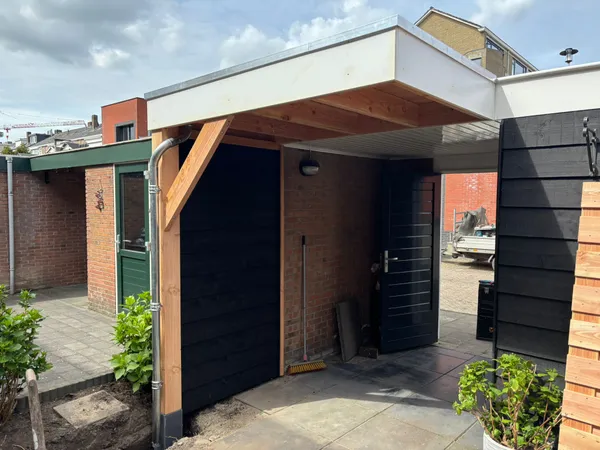 Houten overkapping met cederhouten plafond en zwarte houten wand bij entree.