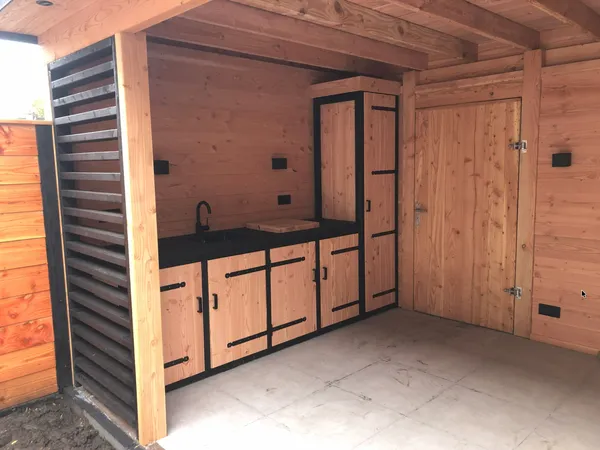 Houten overkapping met ingebouwde buitenkeuken: spoelbak, werkblad en opbergkasten in cederhout met zwart accent.