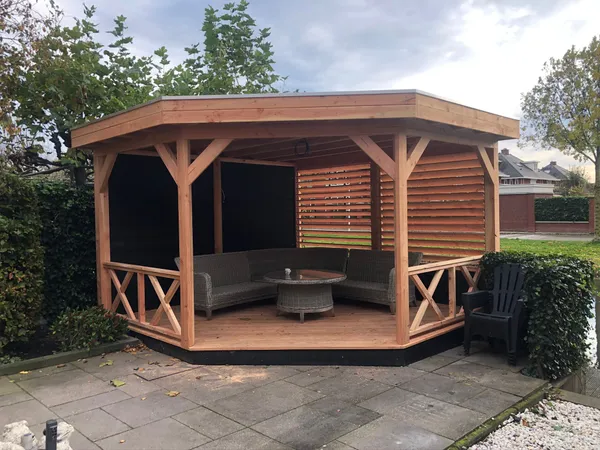 Achthoekige houten overkapping met loungeset en bestrating.