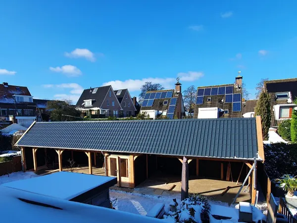Grote houten overkapping met pannendak in besneeuwde achtertuin.