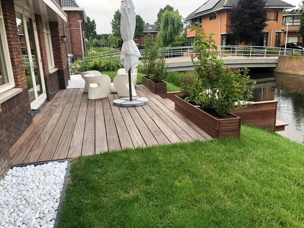 Houten vlonderterras met plantenbakken langs het water.