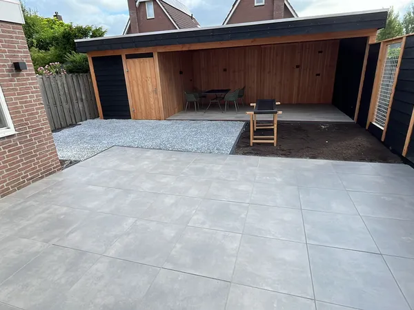 Grote grijze tegelbestrating met houten overkapping op achtergrond.