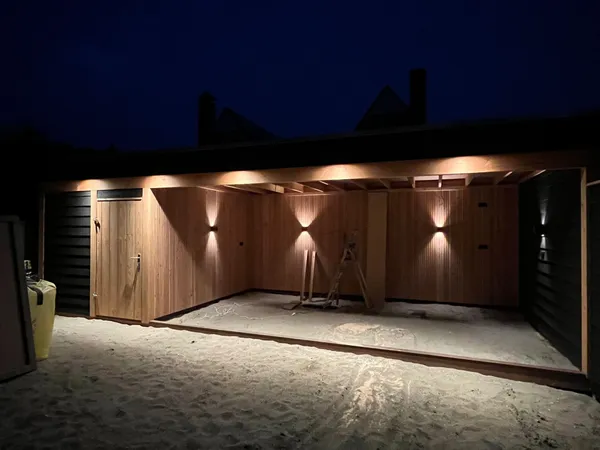 Verlichte houten overkapping bij nacht met cederhouten interieur.