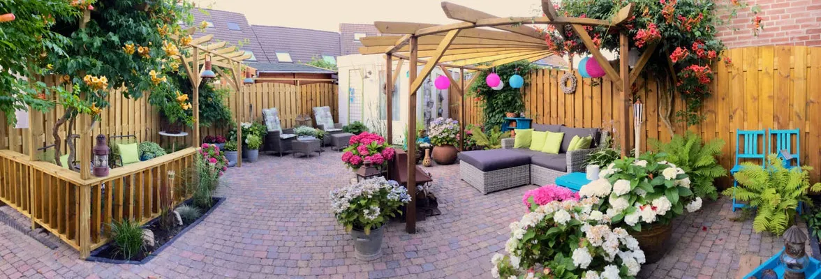 Sfeervolle achtertuin met klinkerbestrating, houten pergola's, schutting en kleurrijke beplanting