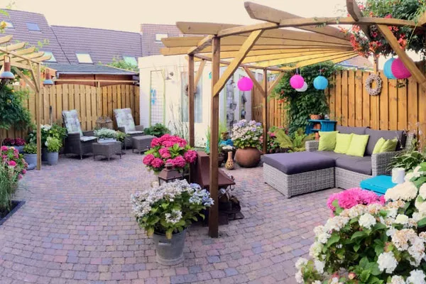 Sfeervolle achtertuin met klinkerbestrating, houten pergola's, schutting en kleurrijke beplanting.