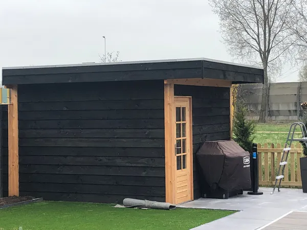 Zwarte houten berging met cederhouten deur naast zwembad.