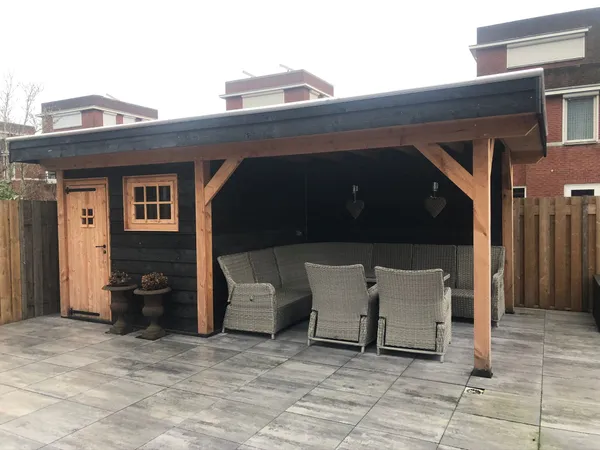 Houten overkapping met loungeset, berging en grijze tegelbestrating.