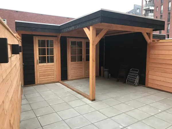 Houten overkapping met grijze tegelbestrating en dubbele bergingsdeuren.