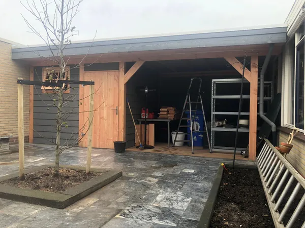 Houten overkapping met opbergruimte en grijze tegelbestrating.