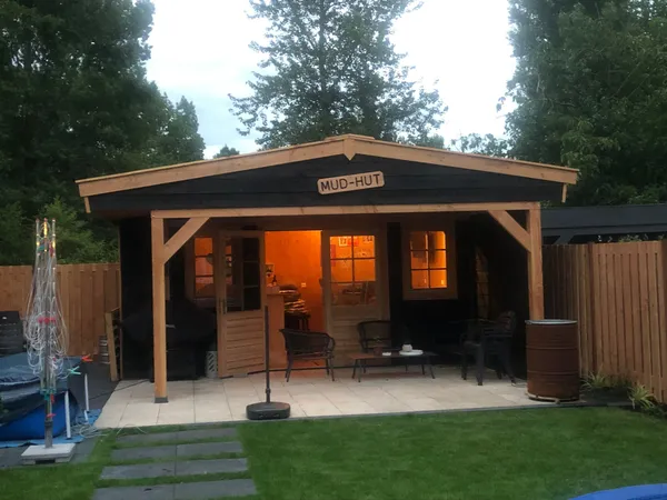 Houten tuinhuis 'Mud-Hut' met overkapt terras en sfeerverlichting.