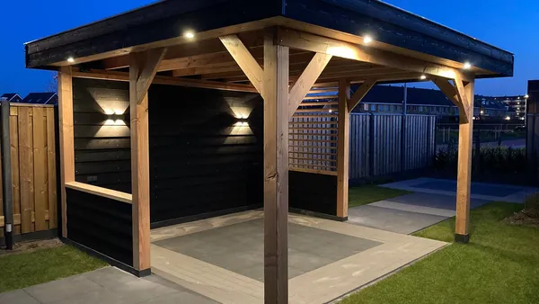 Houten overkapping met inbouwspots en zwart dak bij avondlicht.
