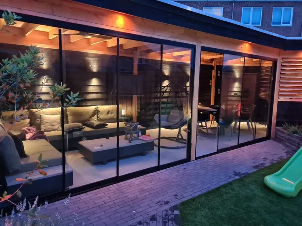 Houten overkapping met glazen schuifwanden en sfeerverlichting.
